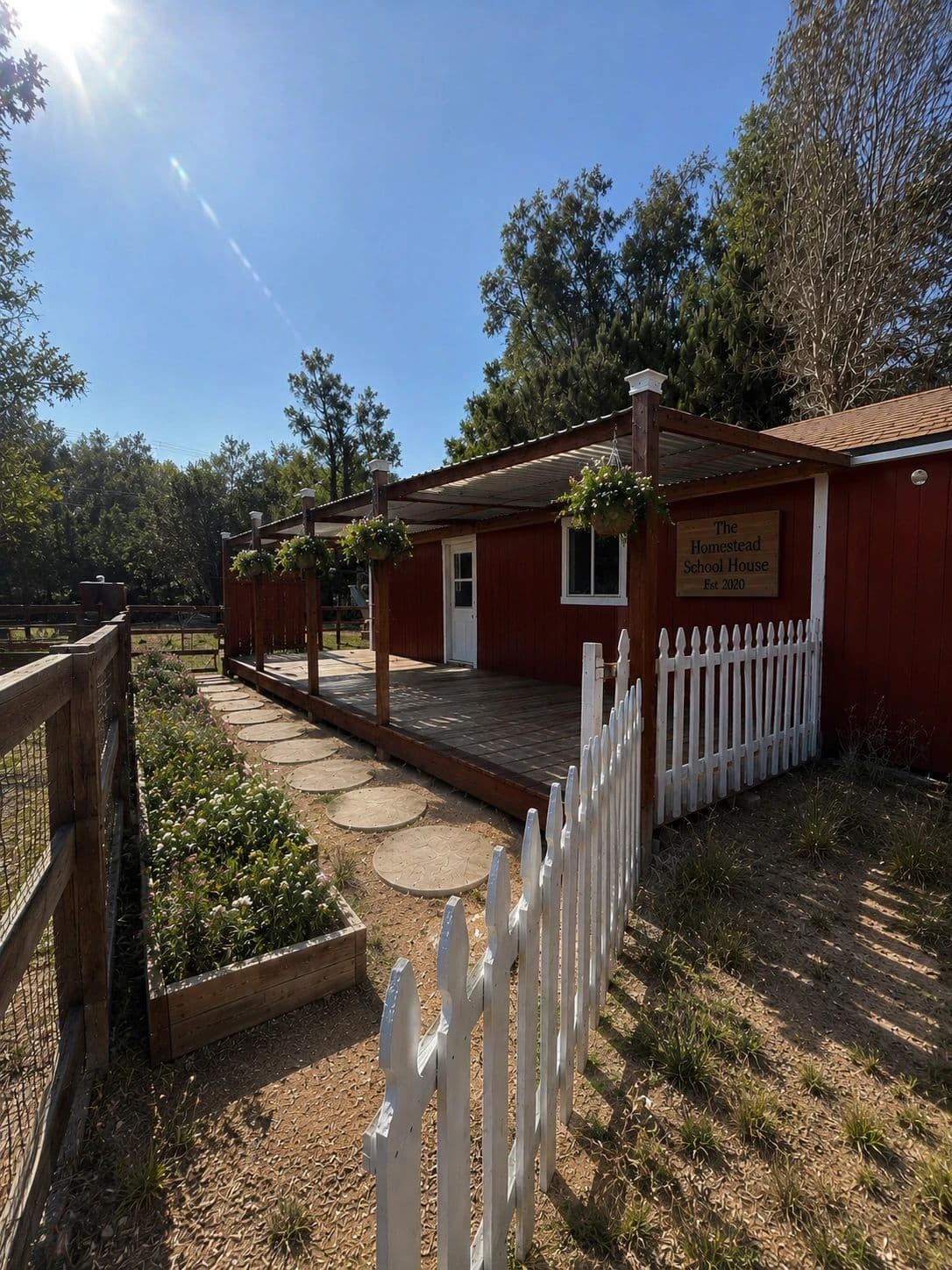 The barn-red schoolhouse with its Est. 2020 sign, white picket fence, hanging flower baskets, and stepping-stone path